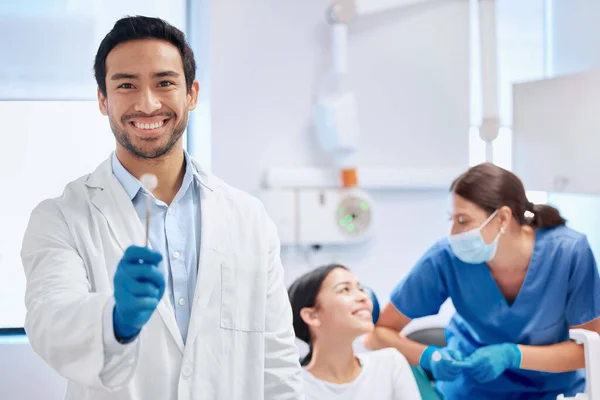 为他的病人提供高质量的工具 当他的助手帮助病人时 一个举起工具的年轻牙医 — 图库照片
