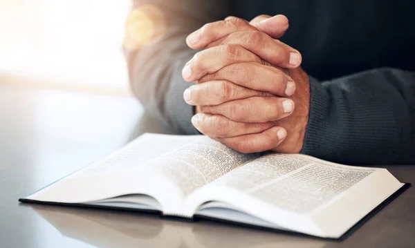 Bible, hands and prayer of a man reading christian text for spiritual healing and religion. Lens flare, hand closeup and praying of a person with peace and a book for praise, support and hope.