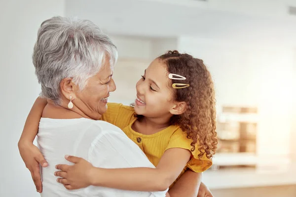 Mixed race grandmother and granddaughter hugging in living room at home. Smiling hispanic girl embracing senior grandparent and bonding in lounge. Happy affectionate elderly woman and child together.