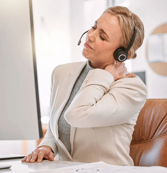 Suffering with a stiff neck. an attractive mature female call center agent suffering with neck pain while working on her computer in the office