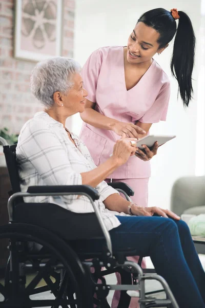 我会为你坚强的 一位年轻的护士与坐在轮椅上的老年妇女分享她的数码平板电脑上的信息 — 图库照片