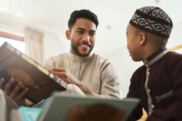 壊れた大人を修復するのではなく 強力な子供を構築します 若いイスラム教徒の男性と息子が自宅のラウンジで読書をしていて — ストック写真