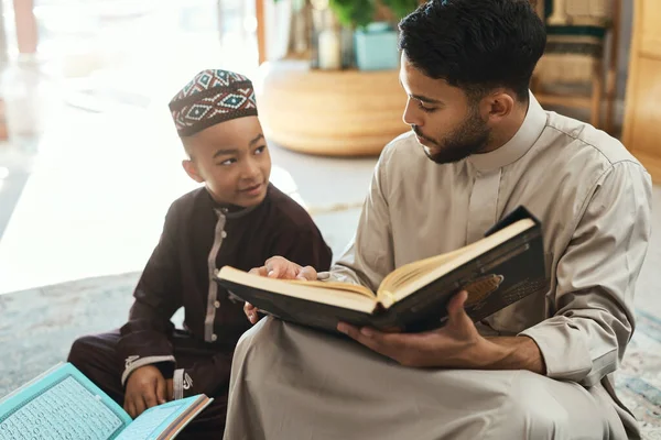 重视孩子就是重视他们 一个年轻的穆斯林男子和他的儿子在家里的休息室看书 — 图库照片