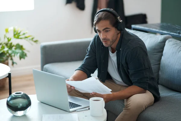 stock image Time to put in the work. a young man doing paperwork while using a laptop at home