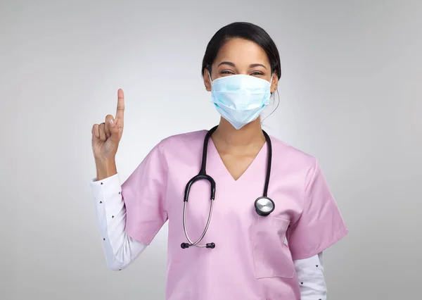 物事は上を見ている 魅力的な若い女性の医療従事者のトリミングされた肖像マスクを着用し 灰色の背景を背景にスタジオでのコピースペースを指して — ストック写真