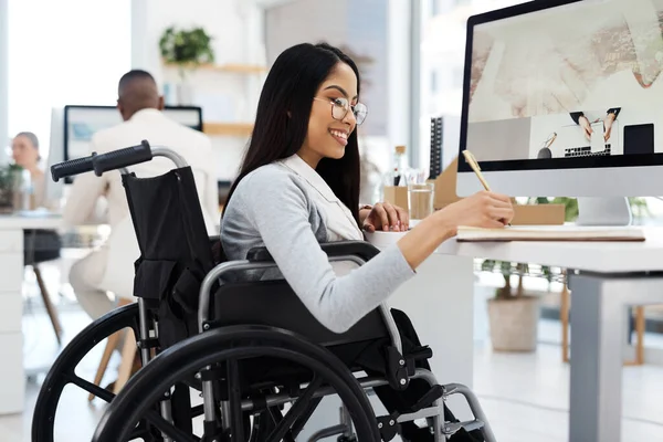 stock image Crossing off things from her to do list. an attractive young businesswoman in a wheelchair writing in her notebook while working in the office