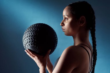 Fitness onun hayatının gerekli bir parçası haline geldi. Spor yapan genç bir kadının mavi arka planda egzersiz topunu tutarken çekilmiş bir fotoğrafı.