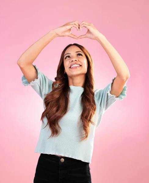 Happy, heart hands and shape with woman in studio for romance, positive and kindness. Love, support and emoji with female and smile isolated on pink background for emotion, hope and gesture.