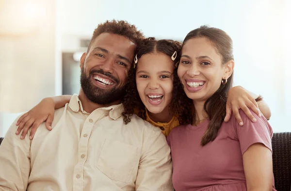 Portrait of mixed race parents enjoying weekend with cute daughter in home living room. Smiling hispanic girl hugging mother and father and bonding in lounge. Happy couple sitting together with child.