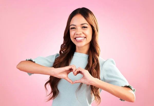 Love, heart hands and portrait of woman in studio for romance, positive and kindness. Peace, support and emoji with female and shape isolated on pink background for emotion, hope and happy gesture.