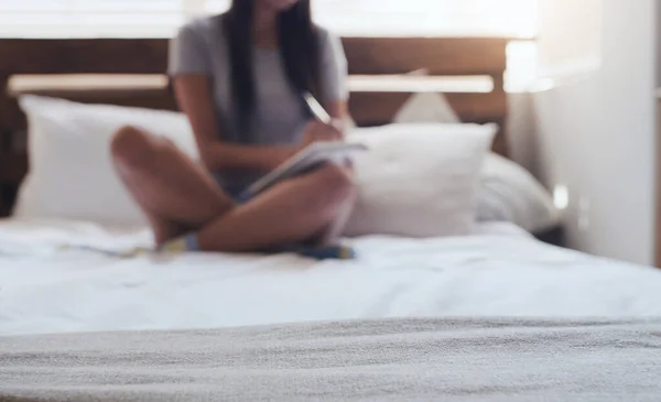 写下让你最快乐的事 一个年轻的女人坐在床上 在家里写日记 — 图库照片