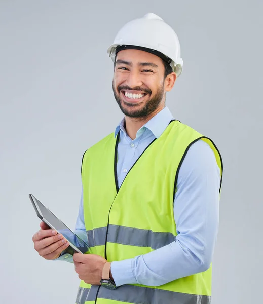 Construction worker, portrait and happy man in studio with tablet and helmet safety on white background. Smile, internet and contractor or architect in online planning for project management in India.