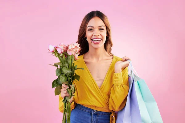 Happy, shopping bags and flowers with portrait of woman in studio for retail, birthday and spring. Event, party and smile with female and roses on pink background for sale, discount and romance.