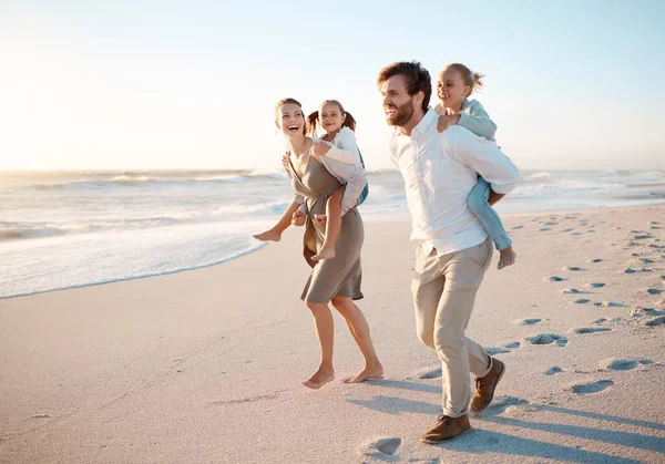 stock image Young family bonding on the beach together. Happy parents having fun with their children on holiday. Little girls playing with their parents on vacation by the sea. Caucasian family on holiday.