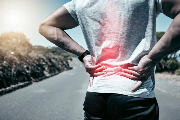 Closeup fit mixed race man holding his back in pain while exercising outdoors. Unrecognizable male athlete suffering with a muscle injury highlighted by glowing cgi. You can get hurt during a workout.