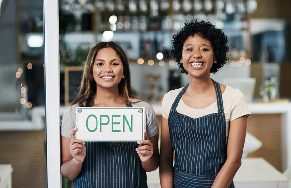 Opening a small business takes a big investment, but its worth it. Portrait of two young women holding an open sign in a cafe