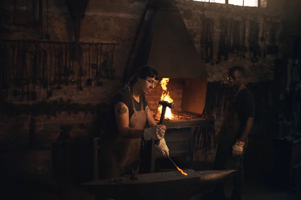 趁热打铁 在铸造厂用铁锤击打热金属棒的年轻女子 — 图库照片