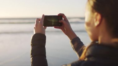 Telefon, sahil ve gün batımında mankenlerle gezmek için fotoğraf çeken bir kadın turist. Su, mobil ve yaz. Bir kadın doğada sosyal medya için bir video kaydediyor..