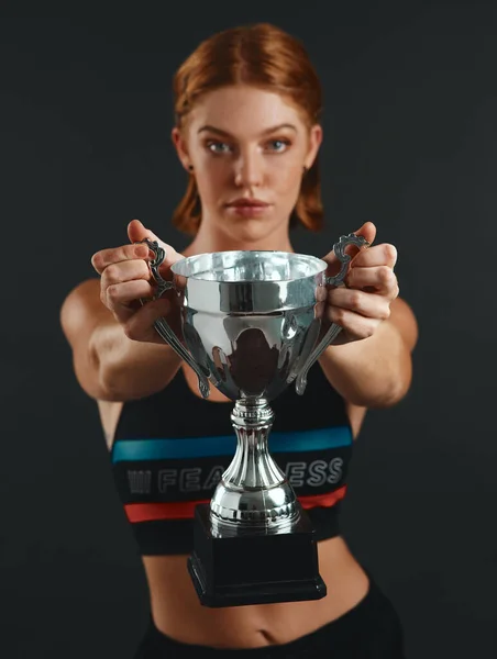Success isnt given, its earned. Studio portrait of a sporty young woman holding a trophy against a black background