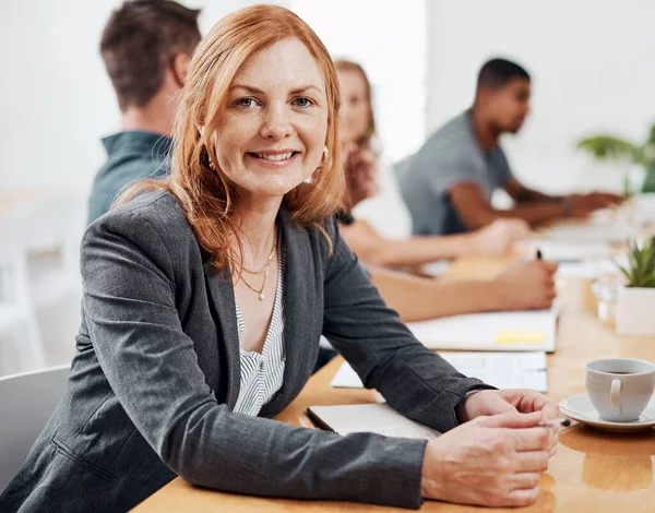 stock image Ive achieved so much while working for this company. Portrait of a mature businesswoman sitting in an office with her colleagues in the background