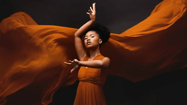 Black woman, art and fashion, fabric on dark background with dance and aesthetic movement. Flowing silk, fantasy and artistic portrait of serious African model in creative designer dress in studio