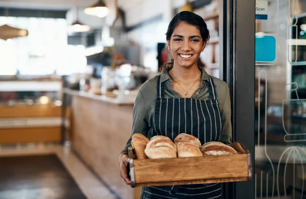 Served fresh just for you. a young woman holding a selection of freshly baked breads in her bakery