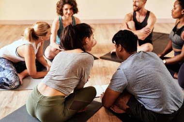 Bu yoga sınıfındaki herkes için bir yer var. Yoga dersi sırasında sohbet eden bir grup genç erkek ve kadın.