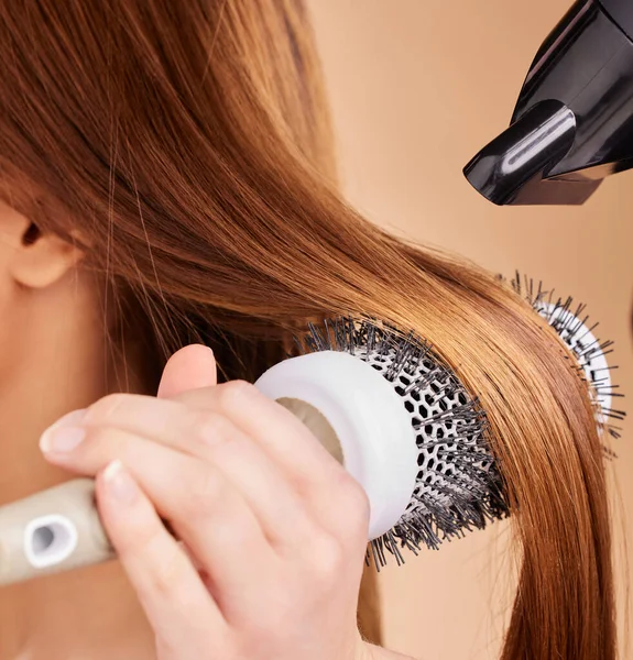 Cabeleireiro secando cabelos loiros à mão com secador de cabelo e escova  redonda em um salão de beleza.