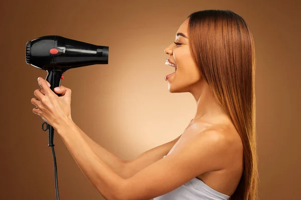 Beauty, styling and hairdryer with woman in studio for hair care, shampoo and grooming. Salon treatment, glow and self care with model isolated on brown background for results, keratin and cosmetics.