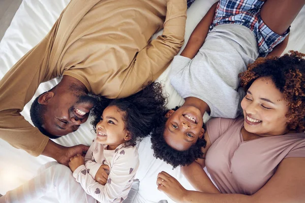 Above, happy and black family laughing in bed, smile and bonding while resting in a home with care. Top view, relax and children waking up with mother and father in a bedroom, playful and having fun.