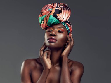 Tahtını kraliçe gibi salla. Gri bir arka planda geleneksel bir Afrika başörtüsü takan güzel bir kadının stüdyo fotoğrafı.