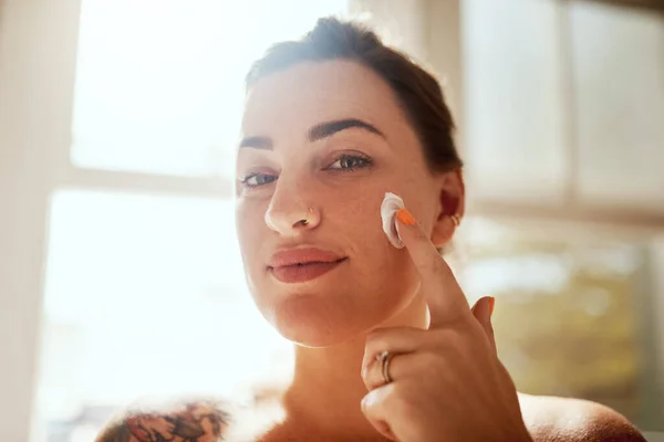 I know what makes my skin glow. an attractive young woman applying moisturiser during her morning beauty routine