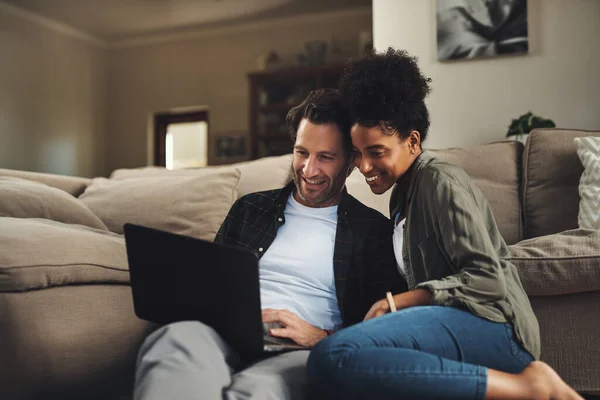 stock image Were both loving this website. a happy young couple using a laptop while relaxing on a couch in their living room at home