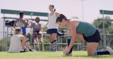 Genç bir bayan sporcu takım arkadaşları arka plandayken ayakkabı bağcıklarını bağlıyor. Hokey oyuncuları antrenmana hazırlanıyor. Aktif sporcu eğitime hazırlanıyor.