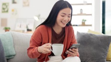 Kahve, cep telefonu ve Asyalı bir kadın sosyal medyada, mobil uygulamalarda ya da internette geziniyor. Rahatla, teknoloji ve kadın evdeki oturma odasında telefonunu kaydırırken cappucino içiyorlar..