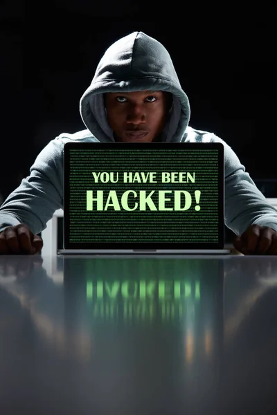 誰があなたの情報を攻撃するか知らない あなたがハッキングされたという言葉でラップトップを使用している若いハッカー — ストック写真