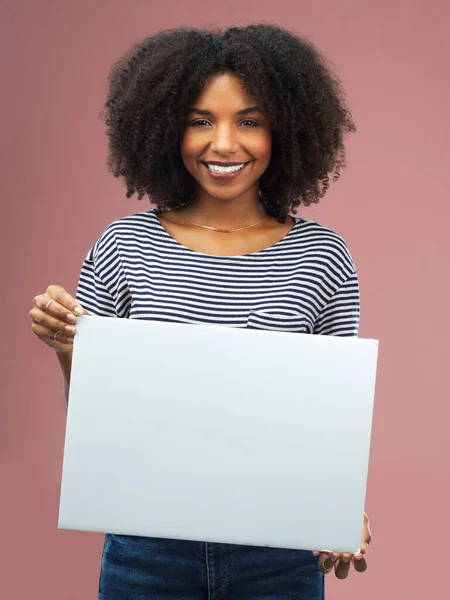 This is for you. Studio shot of an attractive young woman holding a blank placard against a pink background