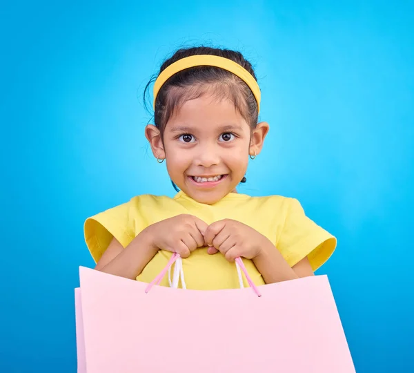生日宴会 活动或庆祝活动中的女孩微笑 肖像和礼品袋 并带着礼物在工作室里 商店的选择 袋子和小孩都在看和小孩在一起的孤立的蓝色背景的礼物 — 图库照片