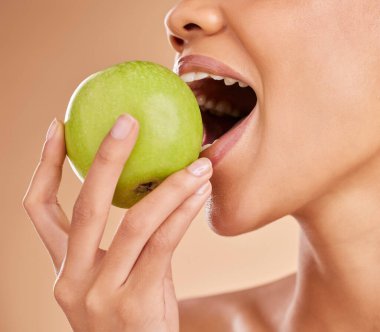 Elma, diş veya ağız sağlıklı beslenme veya temiz diyet için bej arka planda yemek yiyen bir kadın. Isırın, elinizi sıkın ya da sağlıklı olmak için doğal yeşil meyve pazarlayan aç kız reklamcılığını yapın..