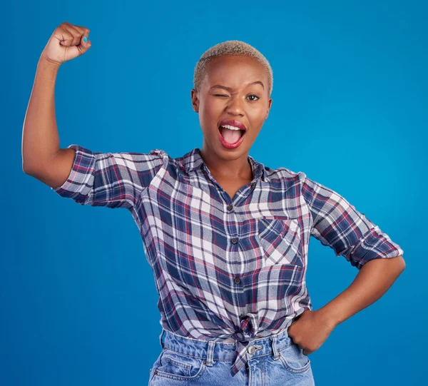 Wink, arm flex and portrait of black woman in studio for empowerment, confident and success. Achievement, hard work and pride with female isolated on blue background for power, strong or motivation.