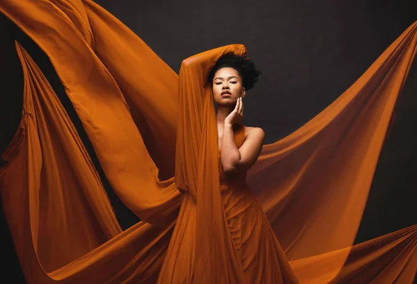 Black woman, art and fashion, flowing fabric on dark background with beauty and aesthetic movement. Silk, fantasy and artistic portrait of serious African model in creative designer dress in studio