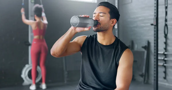 Man, tired and drinking water in gym workout, training and exercise break for energy recovery and muscle rest. Personal trainer, fitness coach and drink for wellness, sports health and weight loss.
