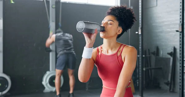 Black woman, rest and drinking water with bottle for fitness, wellness and health in gym. Young female, athlete or healthy lady relax, being thirsty after practice or training for exercise or workout.