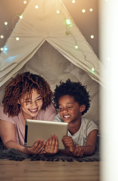 Tablet, black family and mother with kid in tent at night watching movie, video and having fun in home. Technology, love and smile of happy mixed race mom bonding with boy child while streaming film