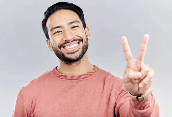 Portrait, smile and Asian man with peace sign in studio isolated on a gray background. Face, v emoji and happy, smiling or excited, young and confident male model with hand gesture or peaceful symbol.