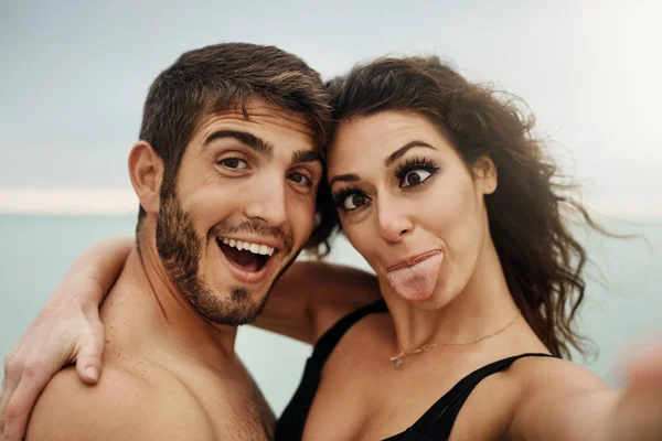 stock image Being silly in love. a young couple taking a selfie at the beach