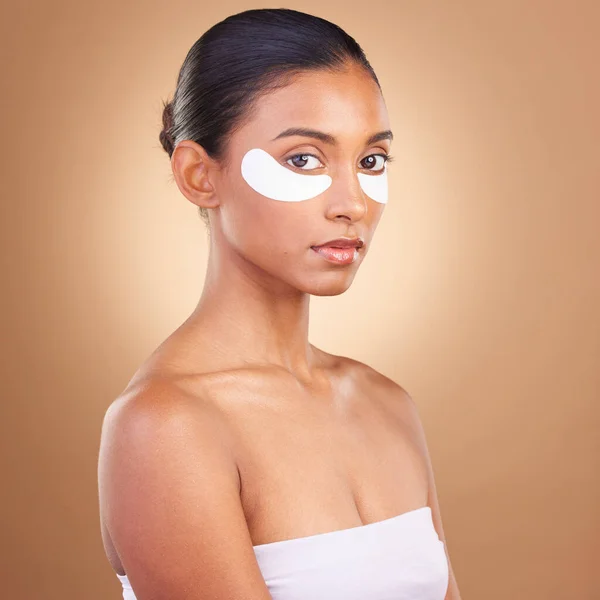 Skincare, eye patch and beauty with Indian woman for facial, spa treatment and glow. Self care, cosmetics and hydration with female model isolated on brown background for mask, product and youth.