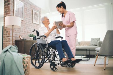 Bütün büyük anlarını kaydettim. Tekerlekli sandalyedeki yaşlı bir kadınla dijital tabletinden bilgi paylaşan genç bir hemşirenin fotoğrafı.