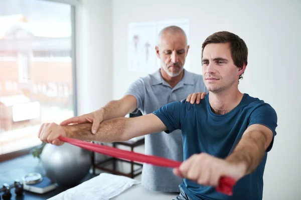 I can feel my body getting better. a handsome mature male physiotherapist helping a patient stretch with resistance bands