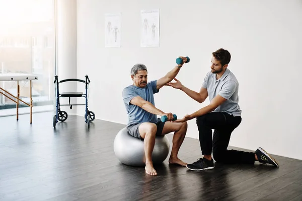 stock image Slow and steady. a young male physiotherapist helping a mature male patient with movement exercises at a clinic